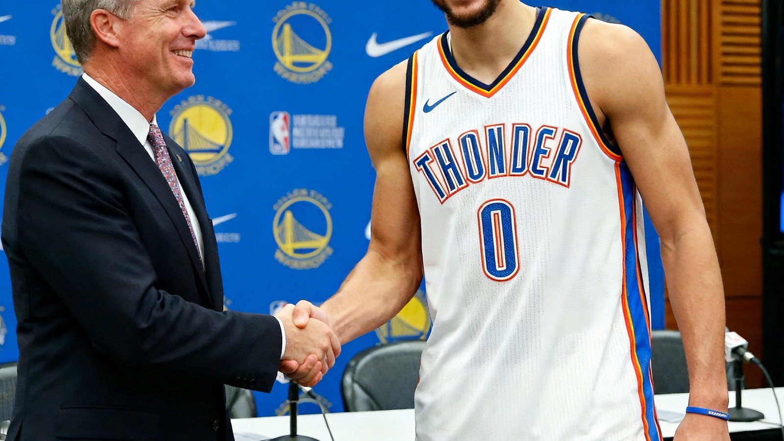 NBA球员在新闻发布会上展示新球队球衣，面带微笑与球队管理层握手